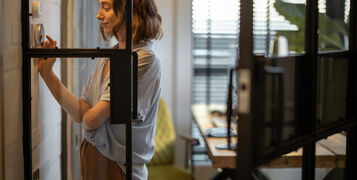 Young,Woman,Controlling,Room,Temperature,With,A,Smart,Thermostat,At